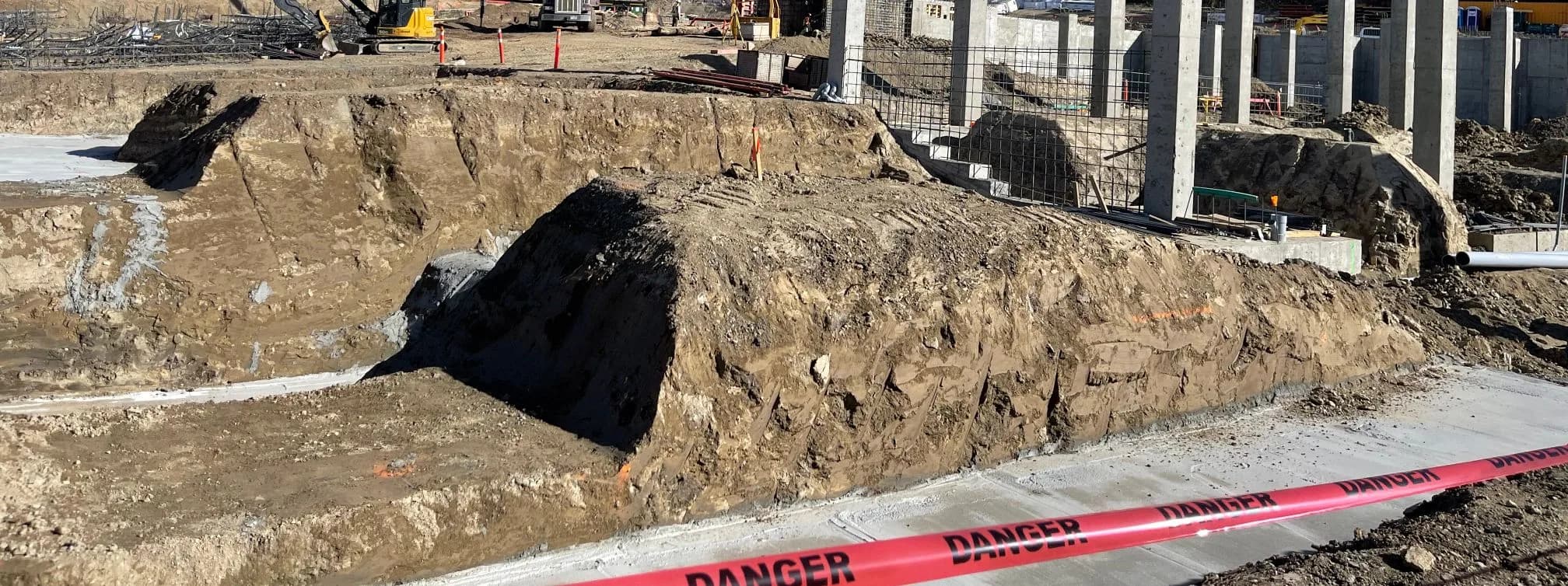 Deep benched foundation excavation beside newly cast concrete walls and columns on an active building site