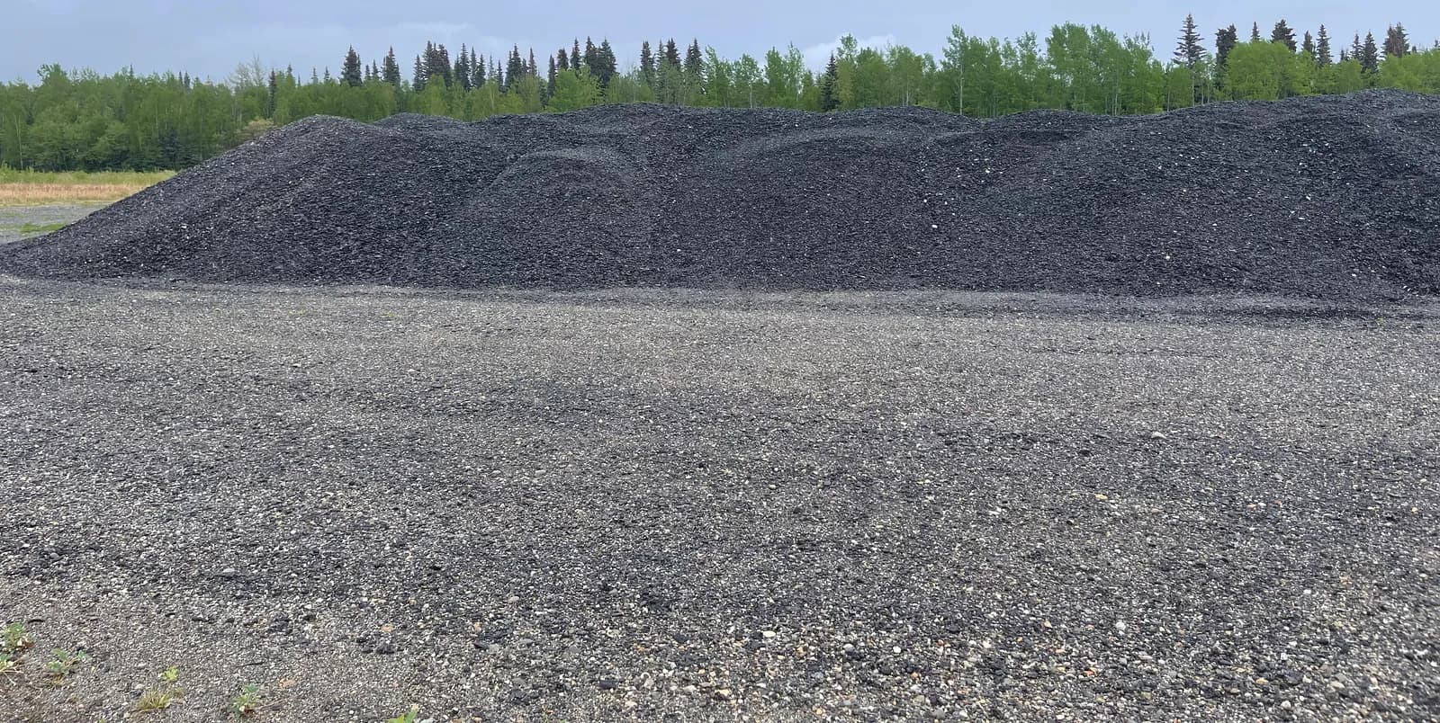 Stockpiles of crushed rock and road base gravel in a Campbell River aggregate yard with forest behind
