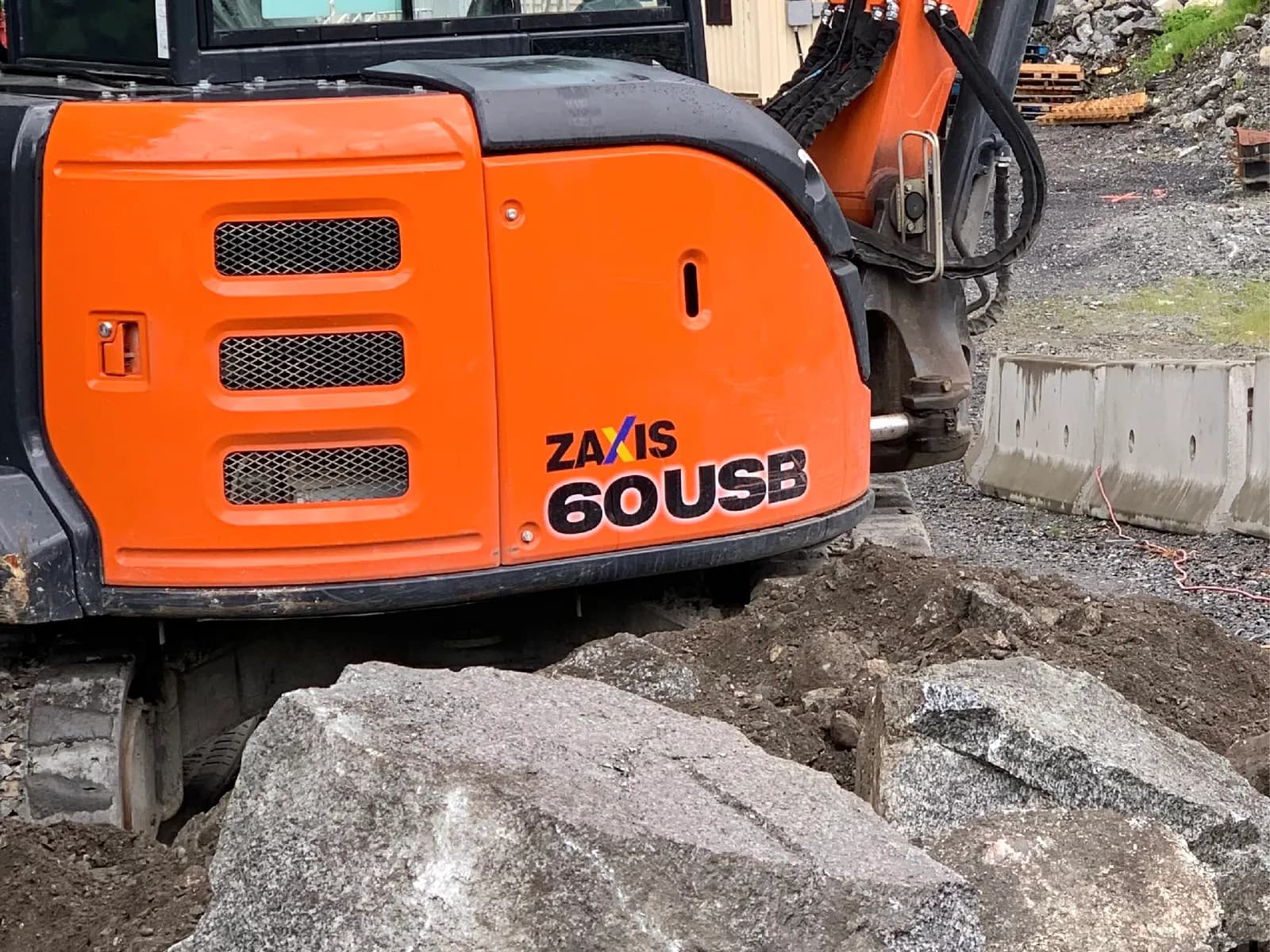 Compact excavator placing large armour rock for a rock retaining wall on a forested Vancouver Island site
