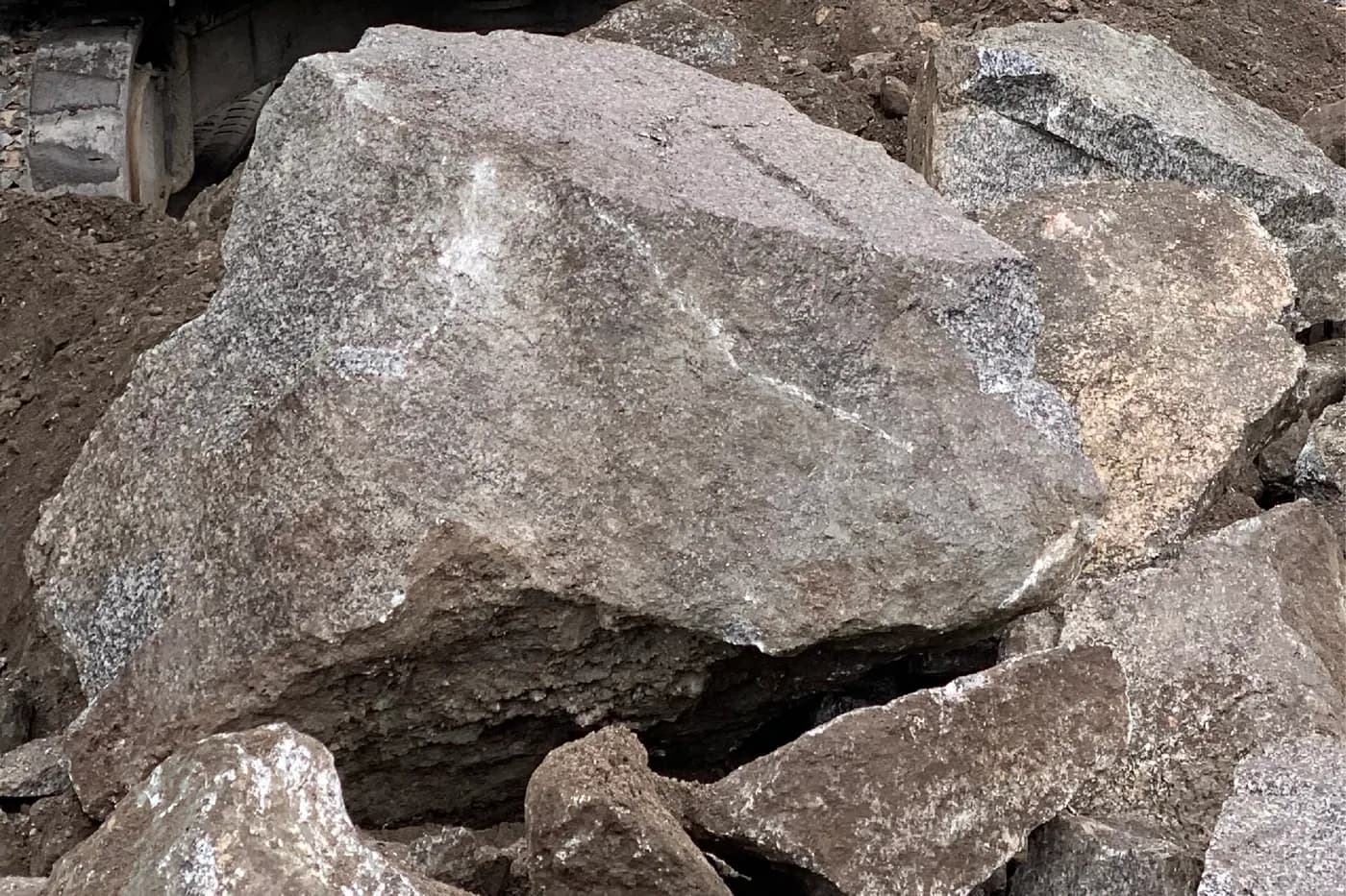 Large angular armour rock staged beside an excavator track for a rock retaining wall