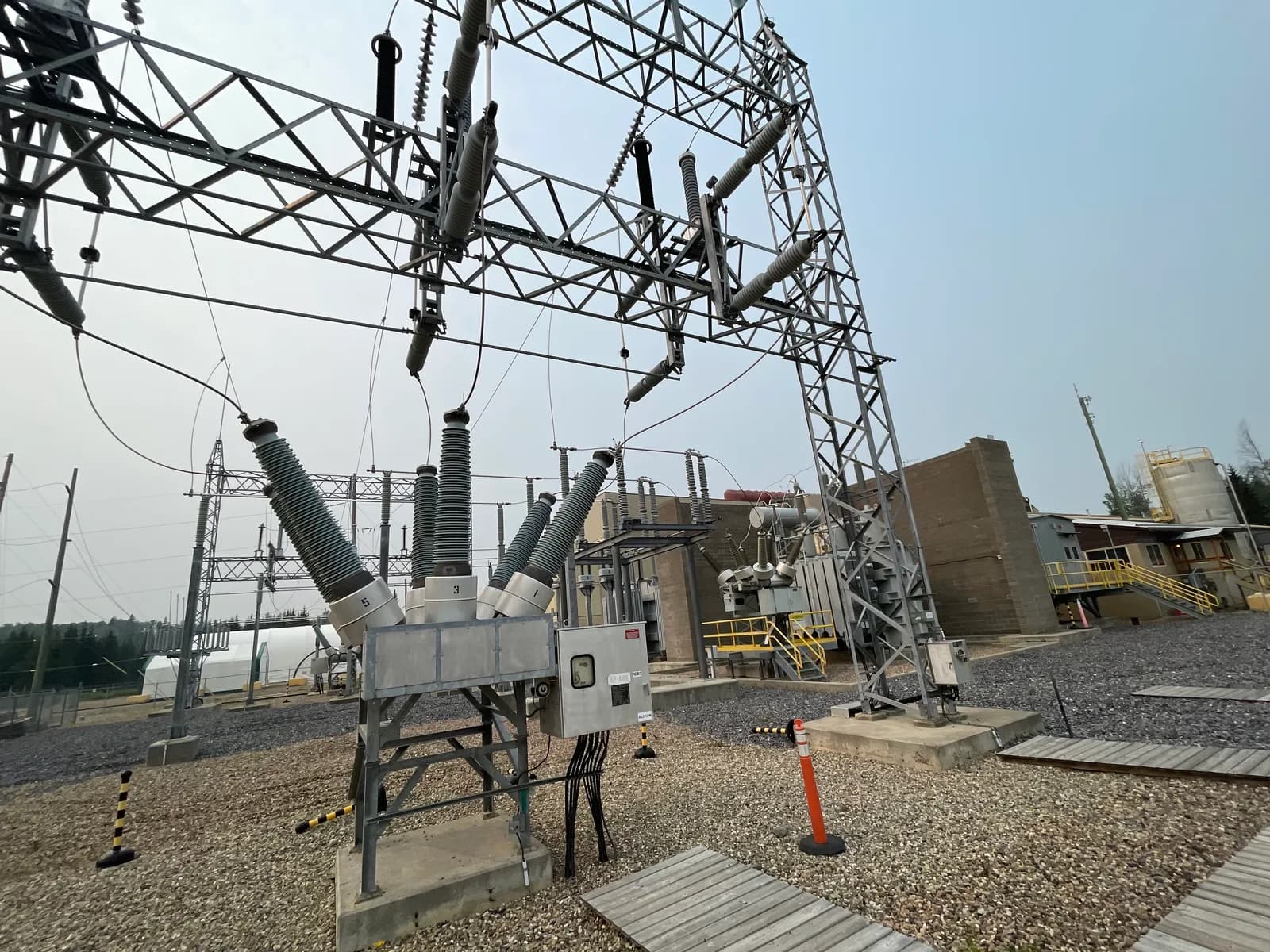 Electrical substation equipment on concrete footings over a crushed-rock yard, with a transformer and control building behind